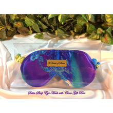 Load image into Gallery viewer, A blue and purple paisley print satin sleep mask. The sleep mask is in a clear acrylic gift box. It is placed on top of white satin with various green plants in the background.