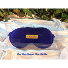 Load image into Gallery viewer, A solid blue satin sleep mask. The sleep mask is in a clear acrylic gift box. There is an A Touch of Satin label on the front of the gift box. It is placed on top of white satin with various green plants in the background.