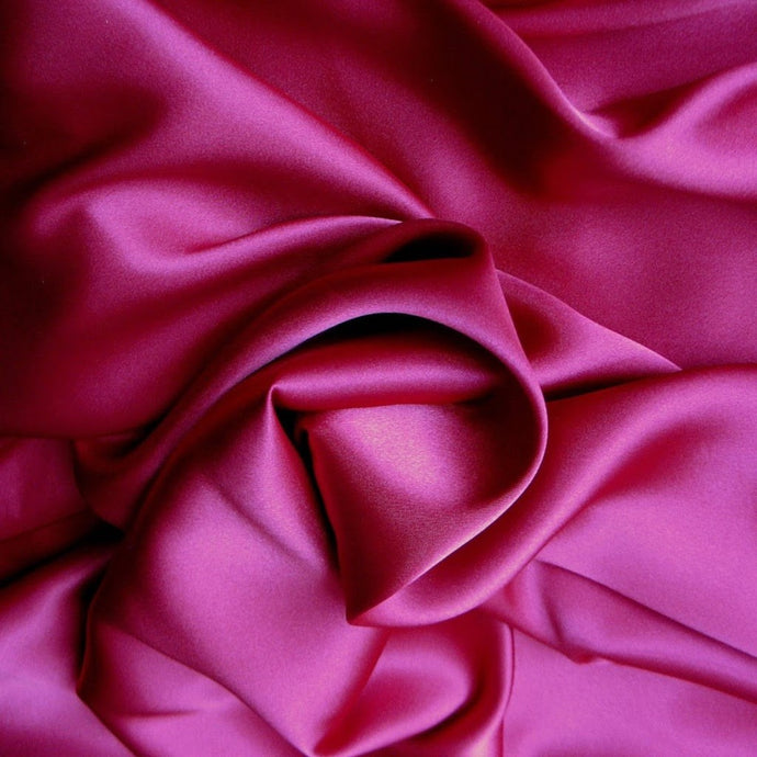 A view from above looking down at magenta color satin material that is swirled.