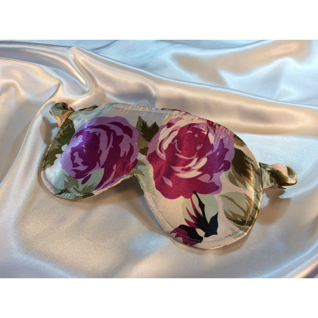 A Green and plum floral print satin eye mask lying on top of white satin sheets. 