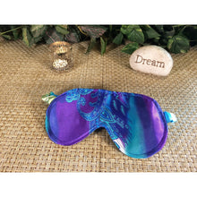 Load image into Gallery viewer, A blue and turquoise paisley print sleep mask. Behind it is a chrome candle holder and a stone with the word "dream" on it. The background has various green plants.