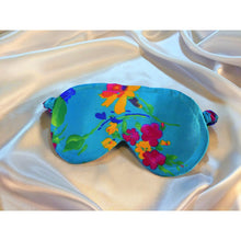 Load image into Gallery viewer, A turquoise blue satin sleep mask with a floral print. The mask is lying on top of white satin sheets.