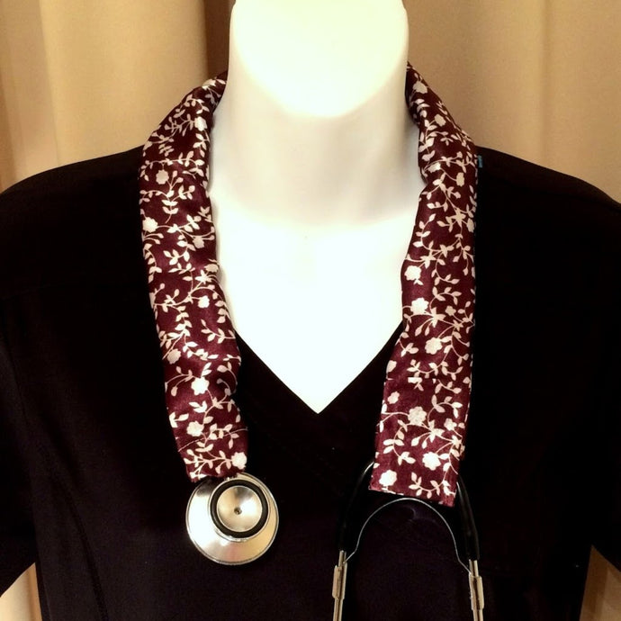 Our EMT stethoscope cover is made from a maroon and white charmeuse satin print. The cover is hanging around the neck of a mannequin.