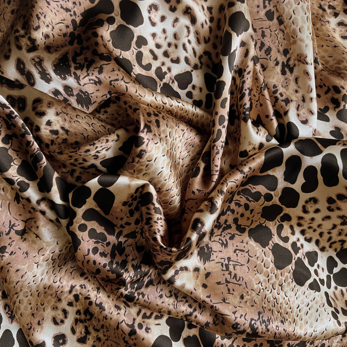 Tan, brown and black satin fabric in a leopard aftrican animal print displayed in a swirl.