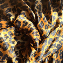 Load image into Gallery viewer, A view from above looking down at satin material in a gold and black leopard animal print.
