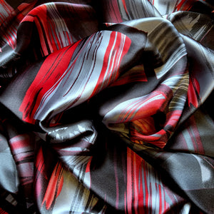Red, black and gray satin fabric in an abstract modern print displayed in a swirl.