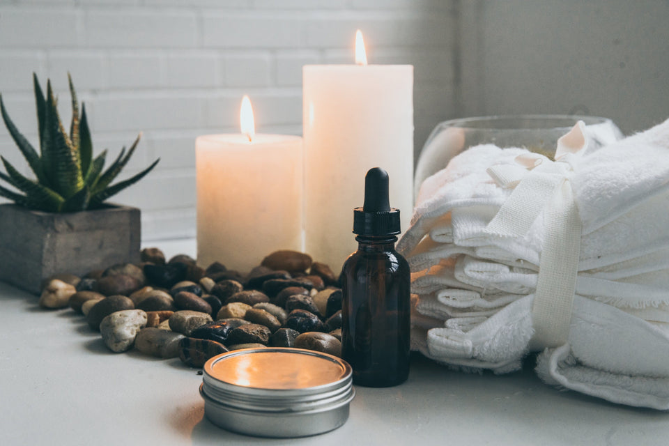 Spa scene with candles burning, a bottle of essential oils, some relaxing stones and white towels.