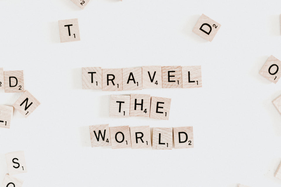 A white scrabble board with the words Travel The World on it.