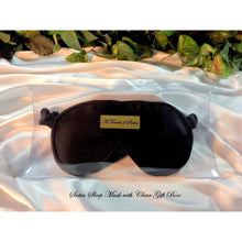 Load image into Gallery viewer, A black satin sleep mask. The sleep mask is in a clear acrylic gift box. It is placed on top of white satin sheet with various green plants in the background. A gold label that says A Touch of Satin is in the middle of the gift box and belowthe gift box are the words &quot;Satin sleep mask with clear gift box&quot;.
