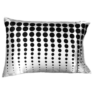 A white satin pillowcase with graduating size black polka dots. Modern, minimalist design. 