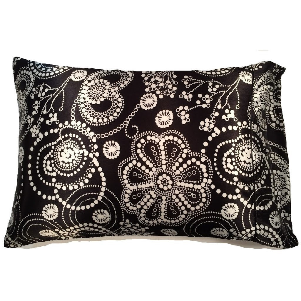 A black satin pillowcase with strands of white pearls and some of the strands are formed to look like flowers.