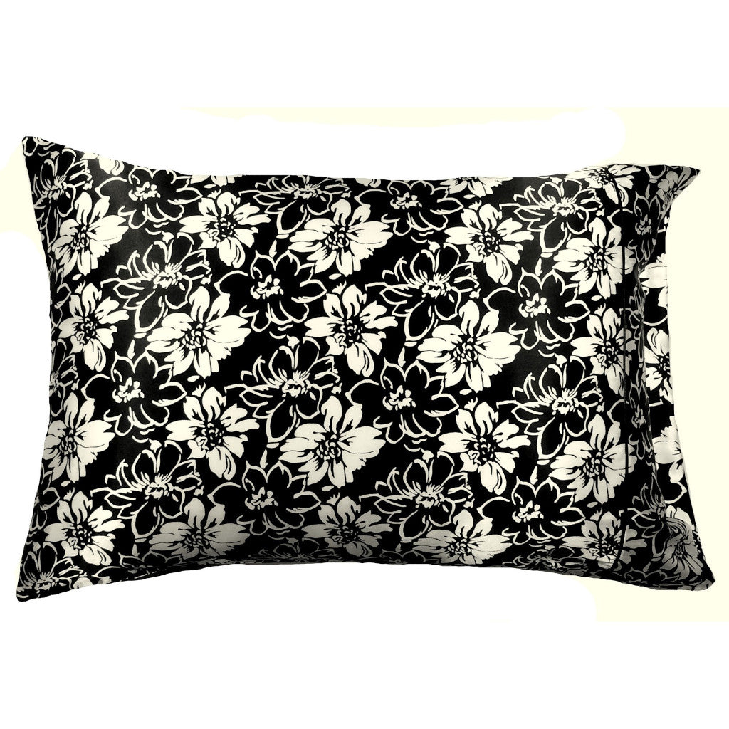 A toss pillow with a black satin cover that has white flowers and white etched flowers on it. The pillow measures 12