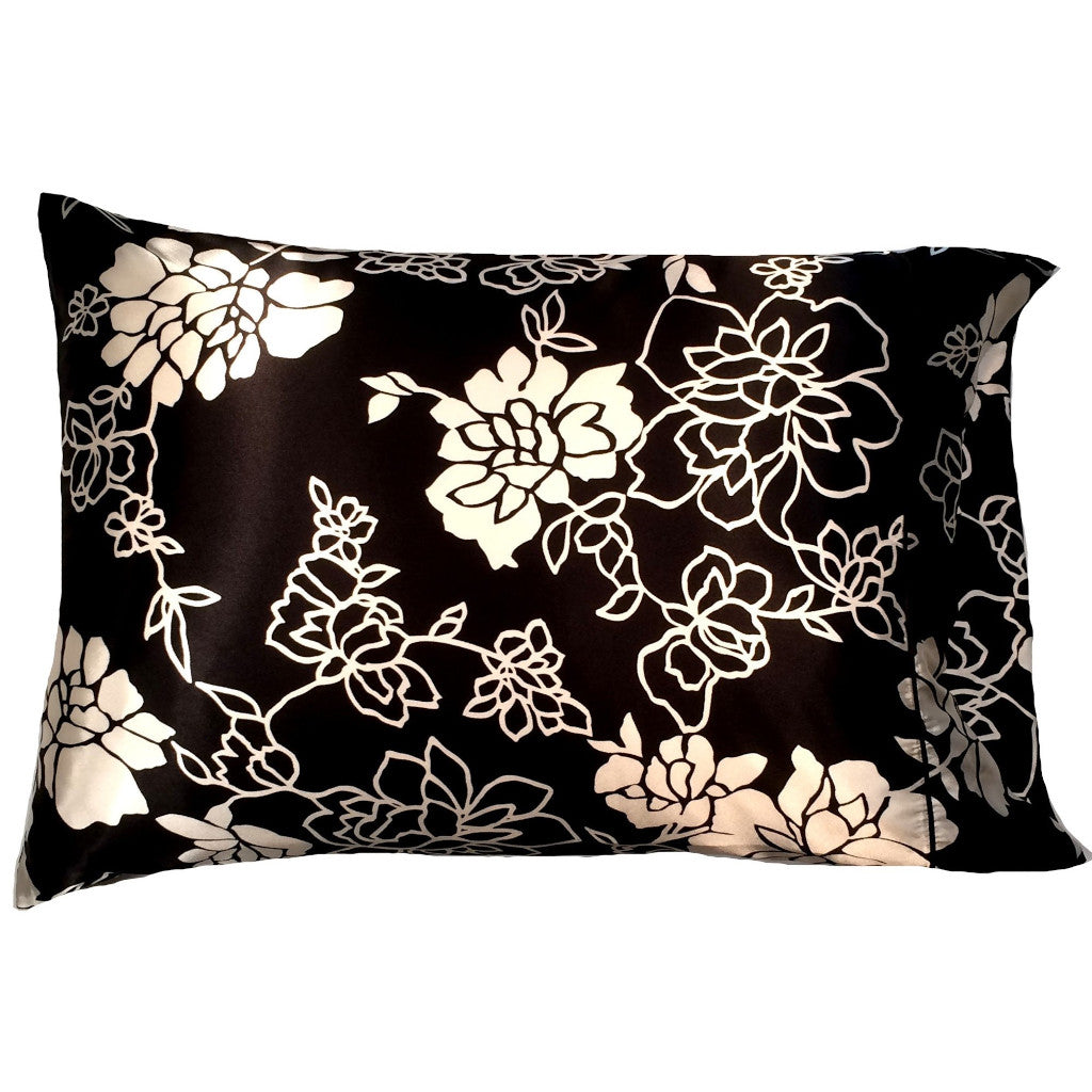 A bedroom pillow with a black cover that has white flowers and white etched flowers on it. The pillow measures 12