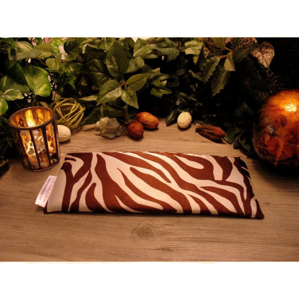 A brown and white zebra print eye pillow. There is a candle burning and various green plants in the background.