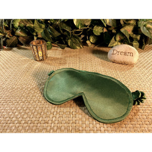 A sage green satin eye shade with an accent candle burning behind it. A stone with the word "dream" is in back of the sleep mask as well.