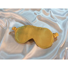 Load image into Gallery viewer, A Gold satin eye mask in laying on top of white satin sheets.
