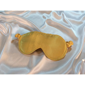 A Gold satin eye mask in laying on top of white satin sheets.