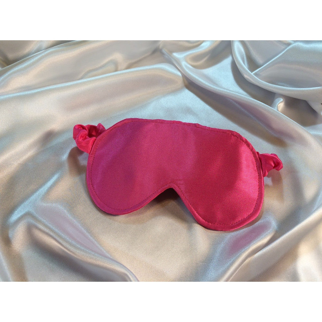 Bubblegum pink eye sleep mask lying on top of white satin sheets.