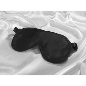 Black satin eye sleep mask on top of white satin sheets.