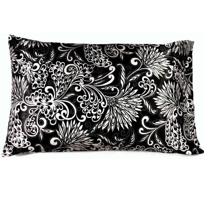 A couch throw pillow with a black satin cover with white flowers on it. The pillow measures 12