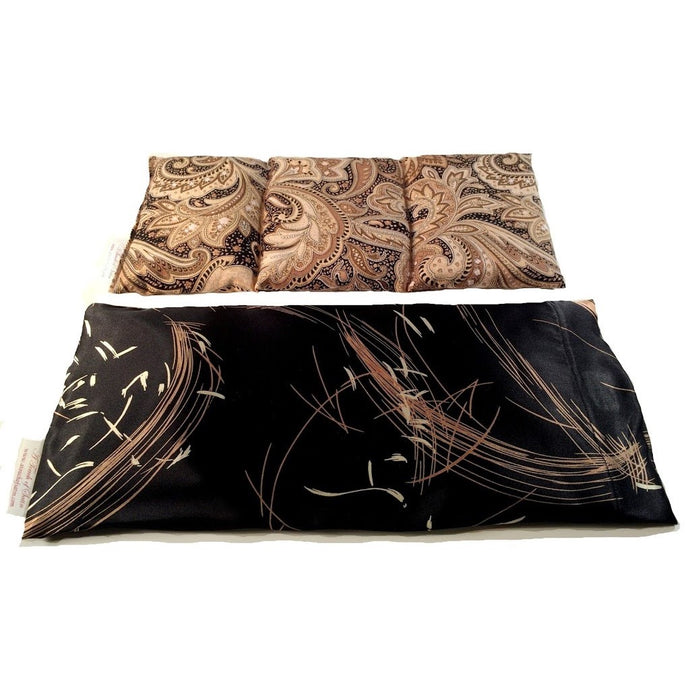 A heating pad with a black satin cover with brown and white wispy strokes. Behind the pad is an insert sewn into three sections. The cover of the insert is a black, gold and brown paisley print.