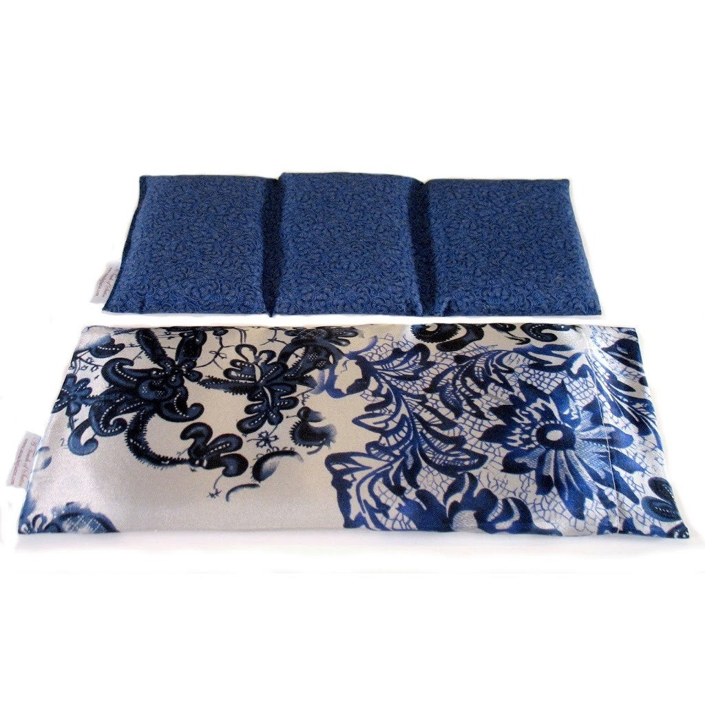 A heating pad with a white satin cover with blue flowers and leaves. Behind the heating pad is a cotton insert sewn in three sections. The cover of the insert is a medium blue and black design.