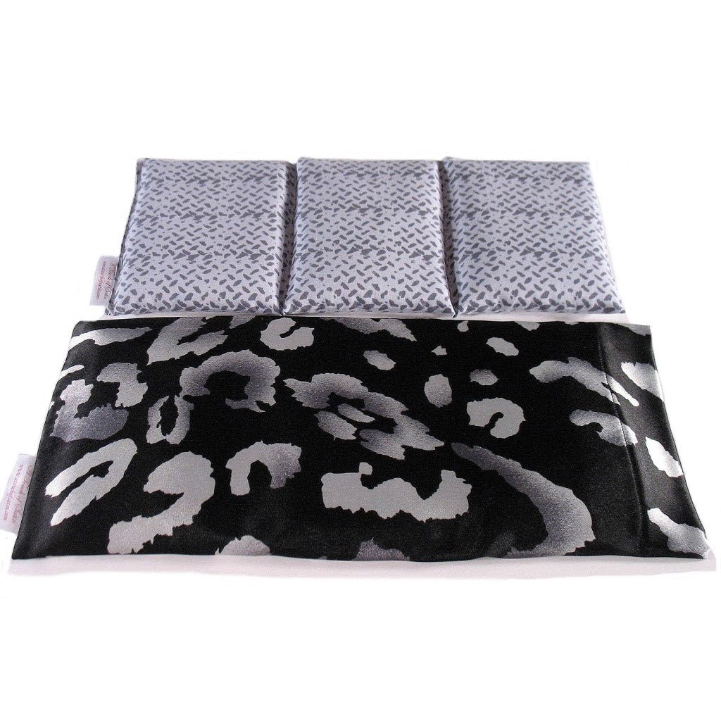 A therapy wrap with a black satin cover with swatches of gray. Behind the wrap is a cotton insert. The insert is sewn in three sections to keep the organic flaxseed in each section. The insert cover is a light and dark gray mix.