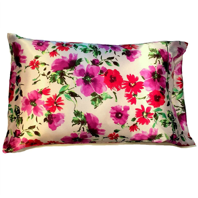 An off white, cream colored satin pillowcase with red and purple flowers and green leaves.